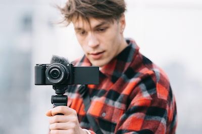 Image of a man holding the base of a camera's grip while looking at the camera's monitor