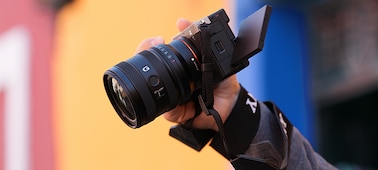 A usage image of a user holding the α7CII with the FE 24-50mm F2.8 G from a high position, showing the compact lens size