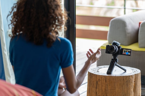 Usage image of female model self-filming with camera mounted on mini tripod on a table and vari-angle screen extended to allow self-view