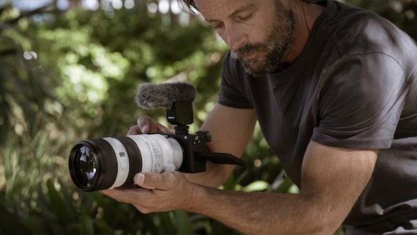 Photo of a man shooting hand-held video with telephoto lens attached