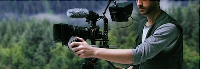 Image showing user with camera on tripod in outdoor environment with microphone, wind shield and external monitor