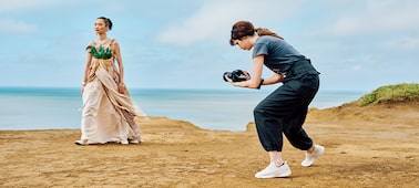 Usage image showing a woman with handheld camera shooting another woman in period costume with coastline in background