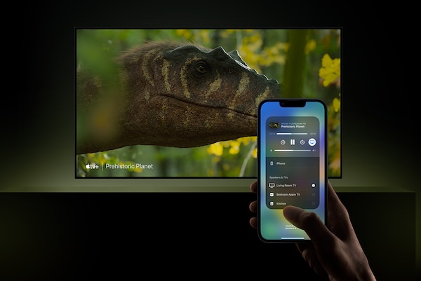 Wall-mounted TV with screenshot of dinosaur head, and hand holding a smartphone in the foreground with app on screen